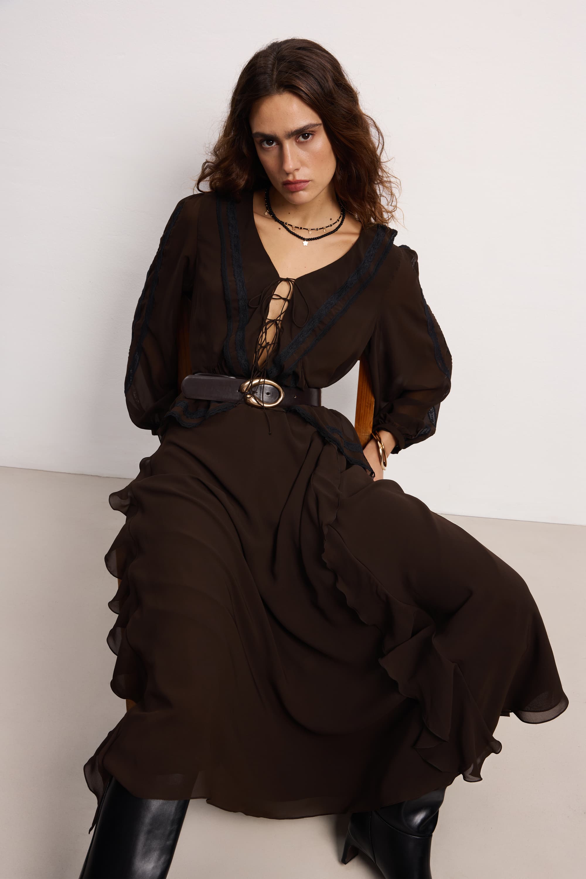 Woman wearing a dark brown Midnight dress with a belt, sitting on a white background