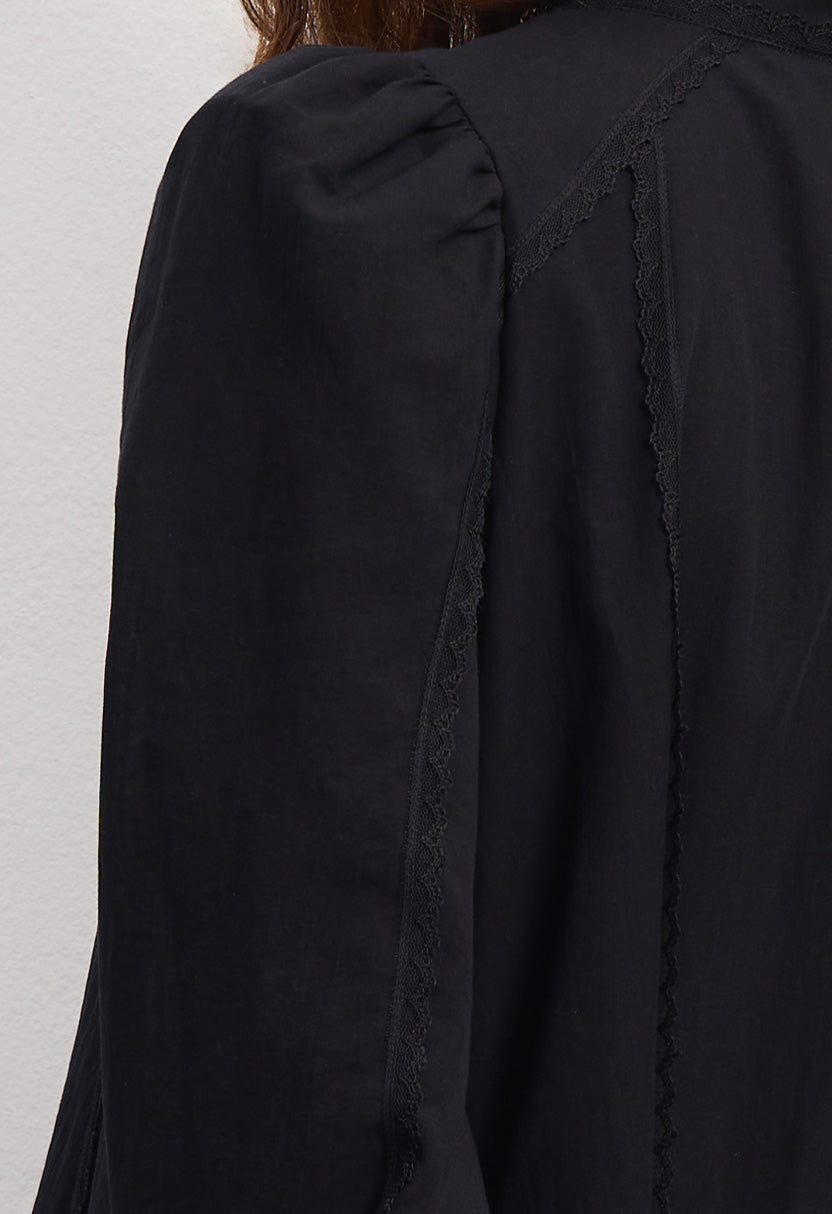 Woman wearing a black Wildflower dress with long sleeves and lace details against a plain background, details front view