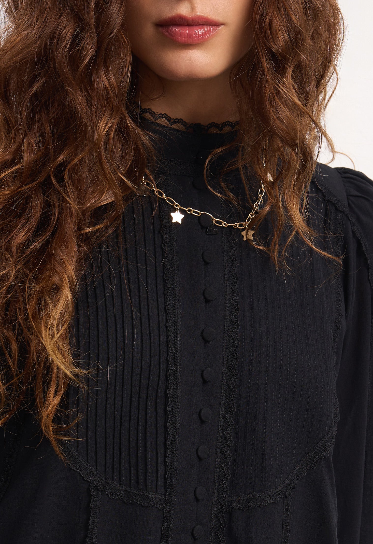 Woman wearing a black Wildflower dress with long sleeves and lace details against a plain background, details front view