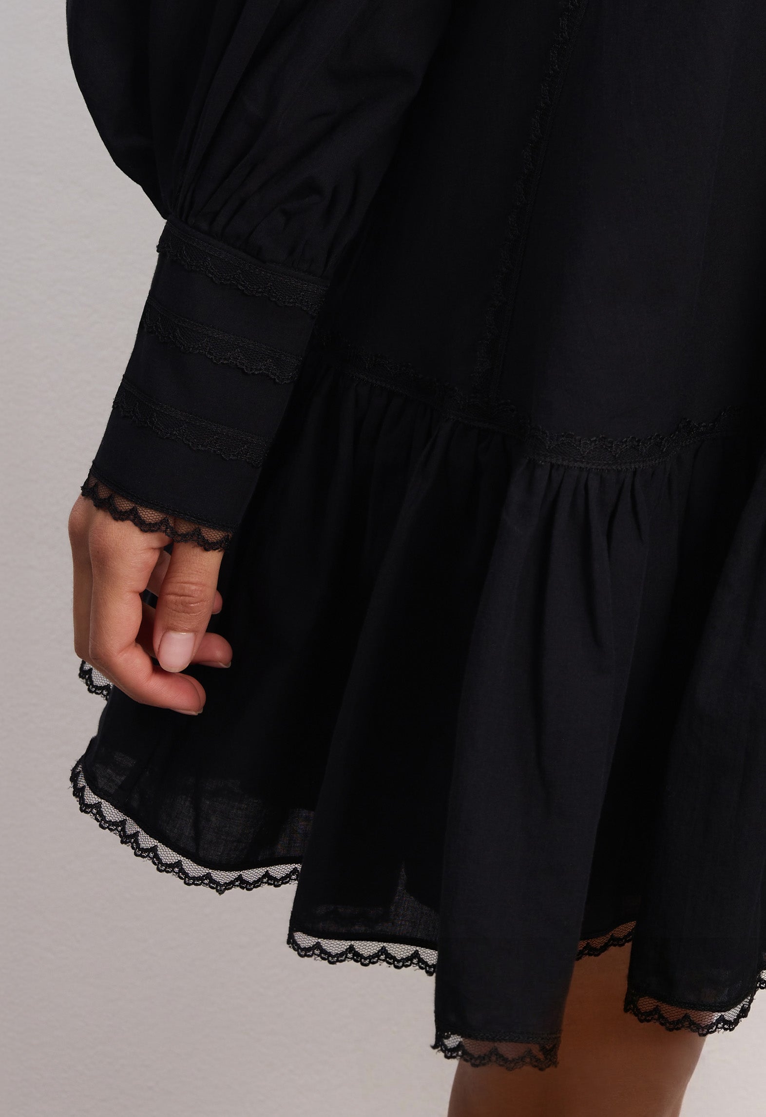 Woman wearing a black Wildflower dress with long sleeves and lace details against a plain background, details front view
