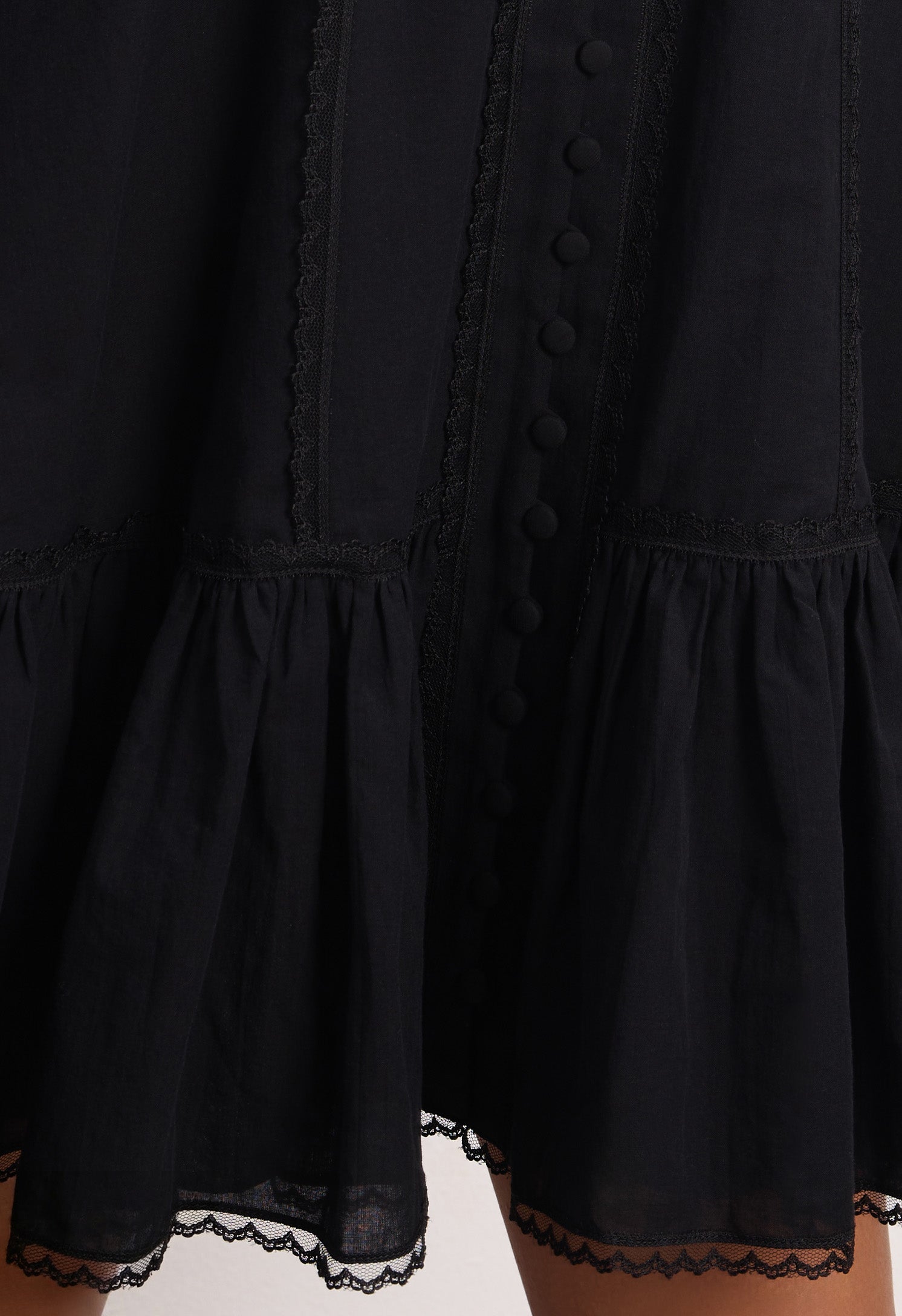 Woman wearing a black Wildflower dress with long sleeves and lace details against a plain background, details front view