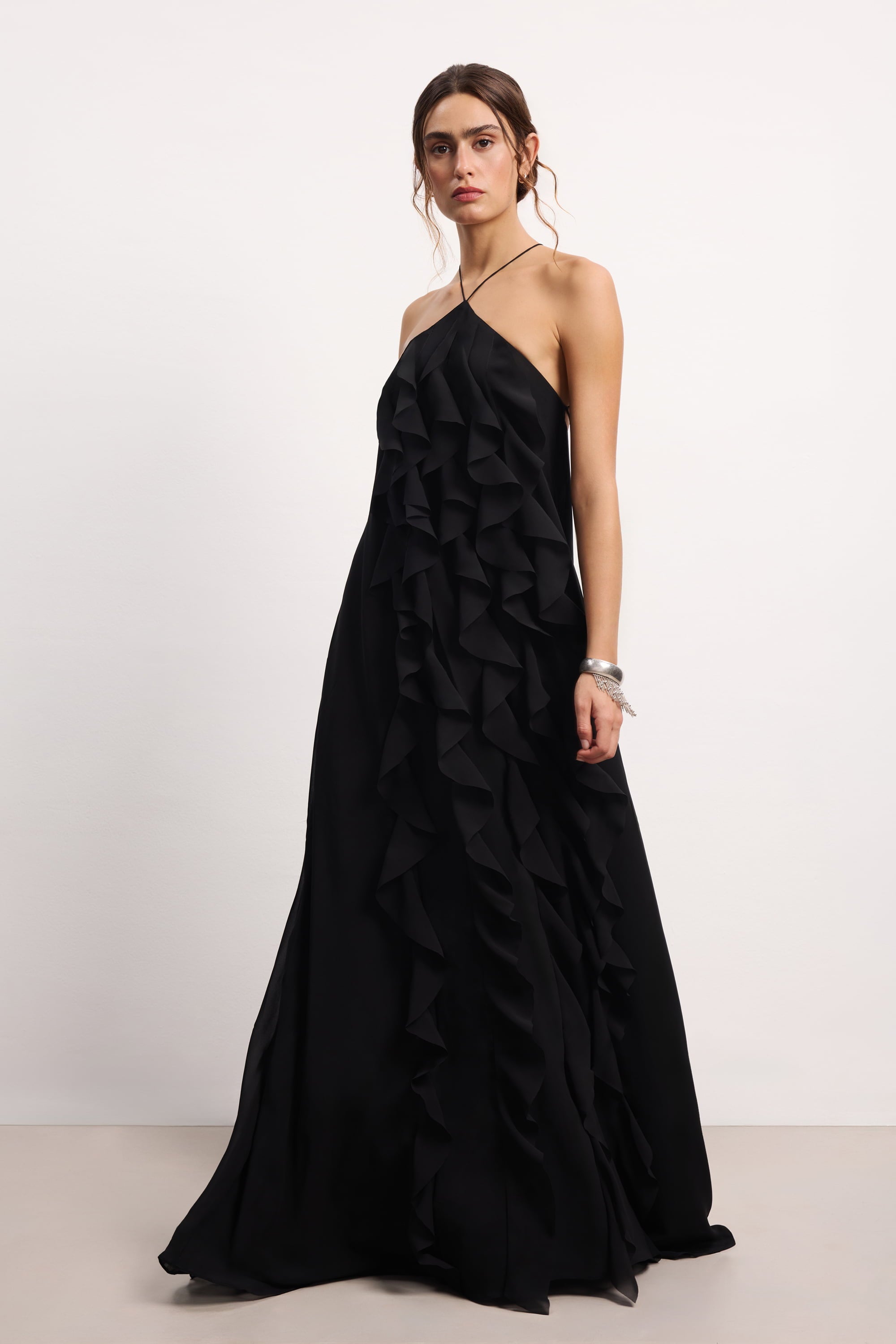 Woman wearing a black halter neck Illusion dress with thin straps and ruffled layers on a white background, side view