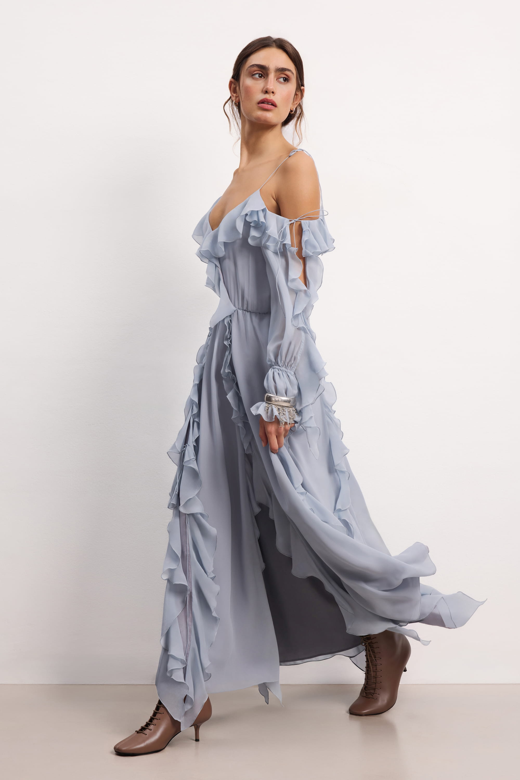 Woman wearing a blue fog off-shoulder ruffled Morning Forest midi dress on a white background, side view