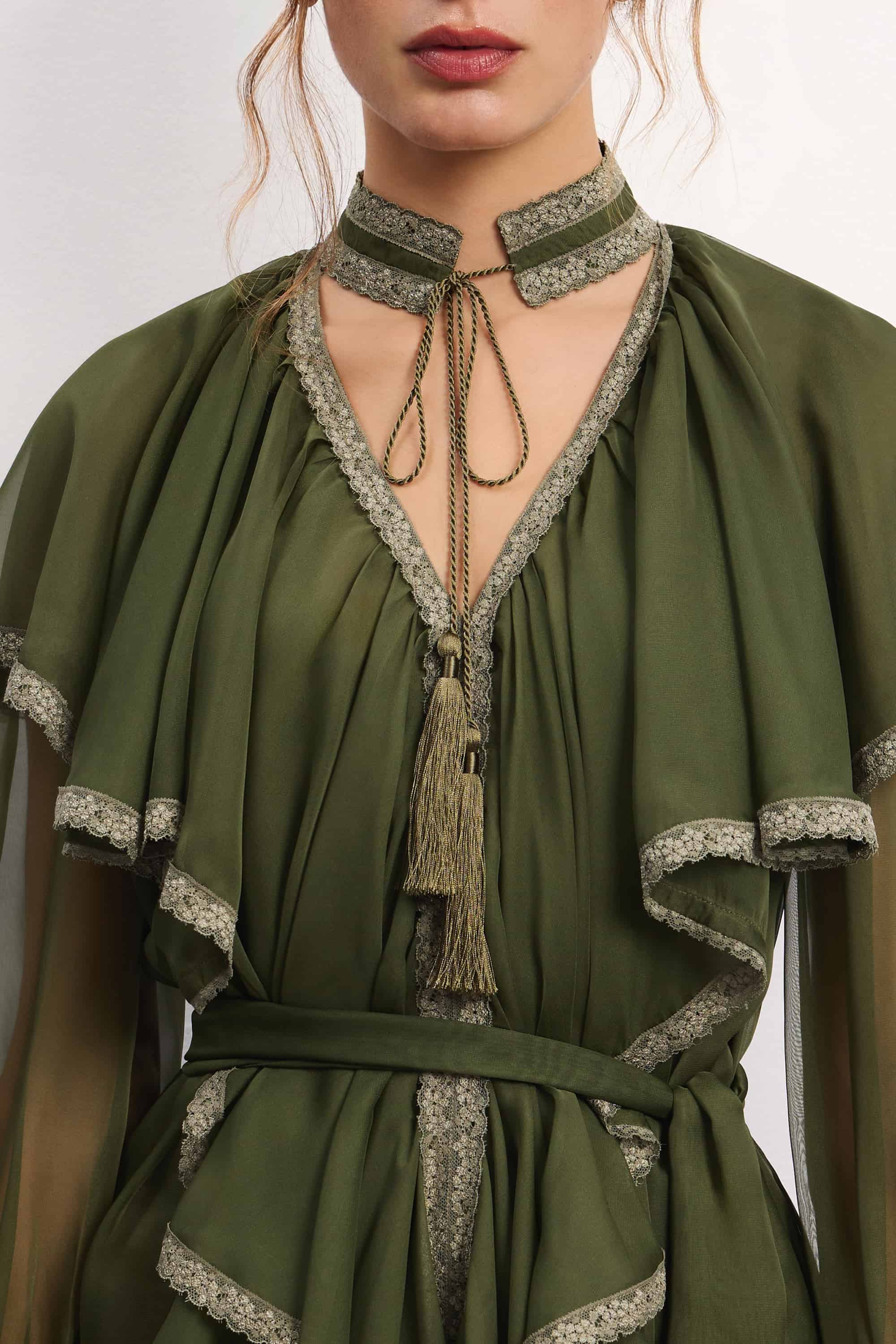 Woman wearing a olive ruffled Ocean Of Tenderness midi dress with black knee-high boots against a white background, details front view