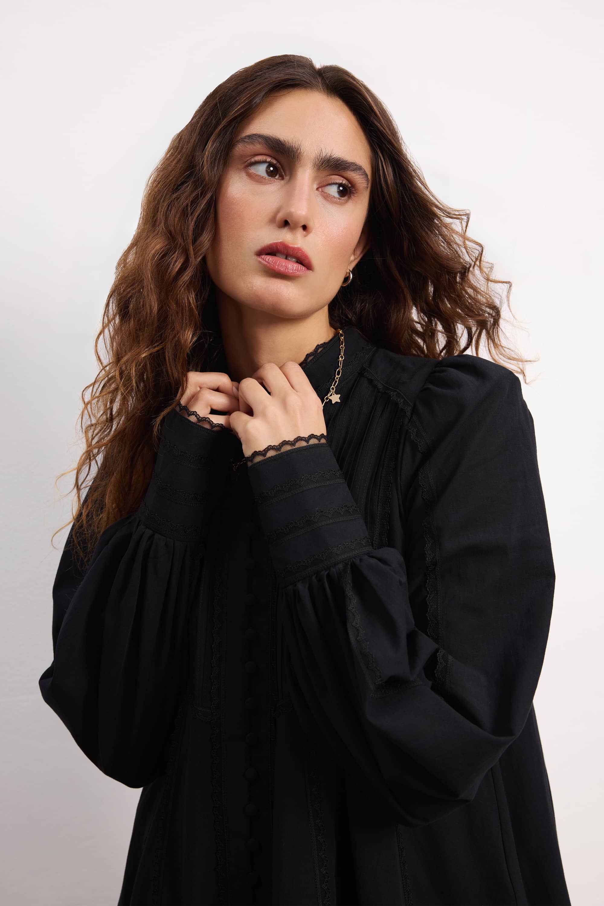 Woman wearing a black Wildflower dress with long sleeves and lace details against a plain background, details front view