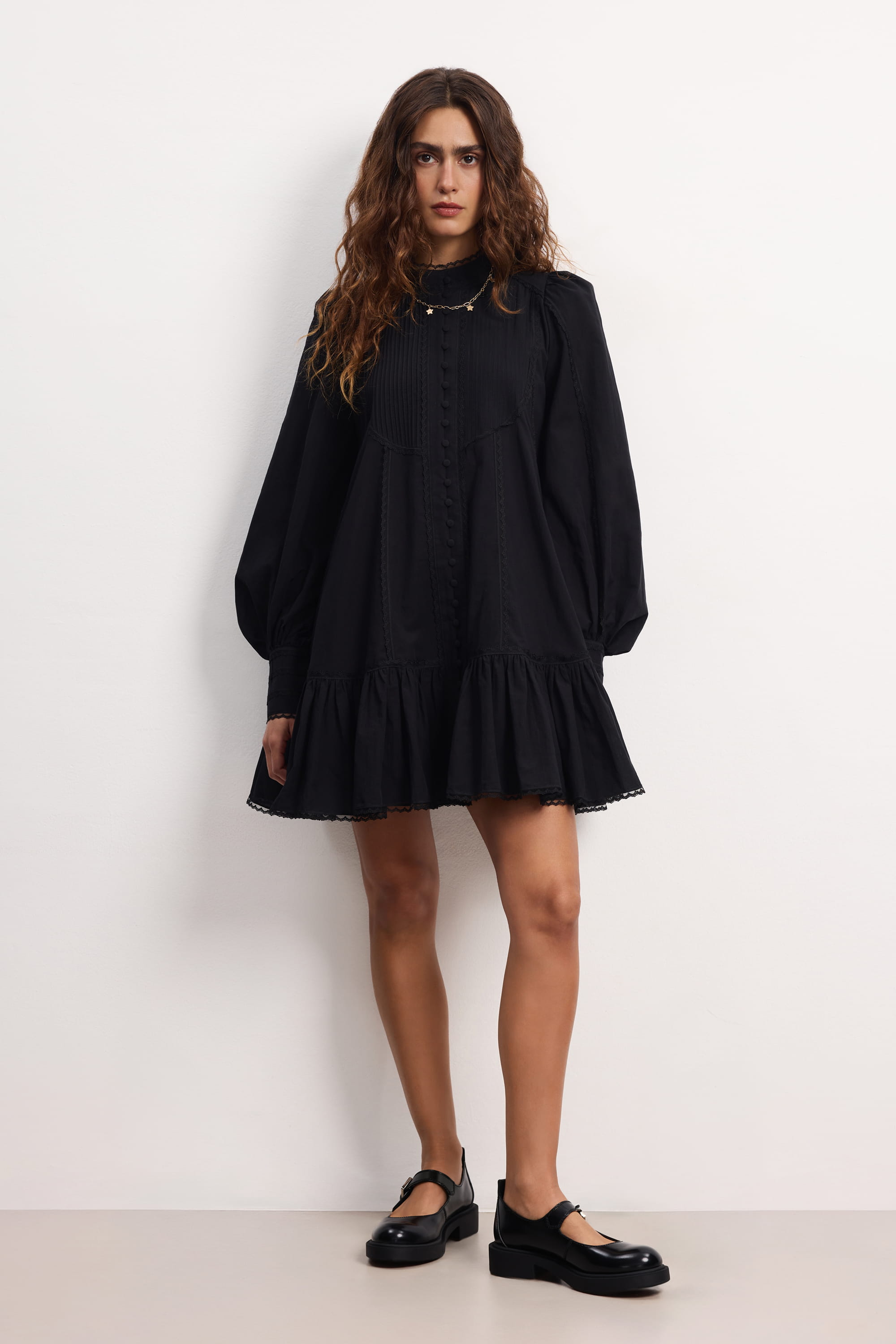 Woman wearing a black Wildflower dress with long sleeves and lace details against a plain background, front view