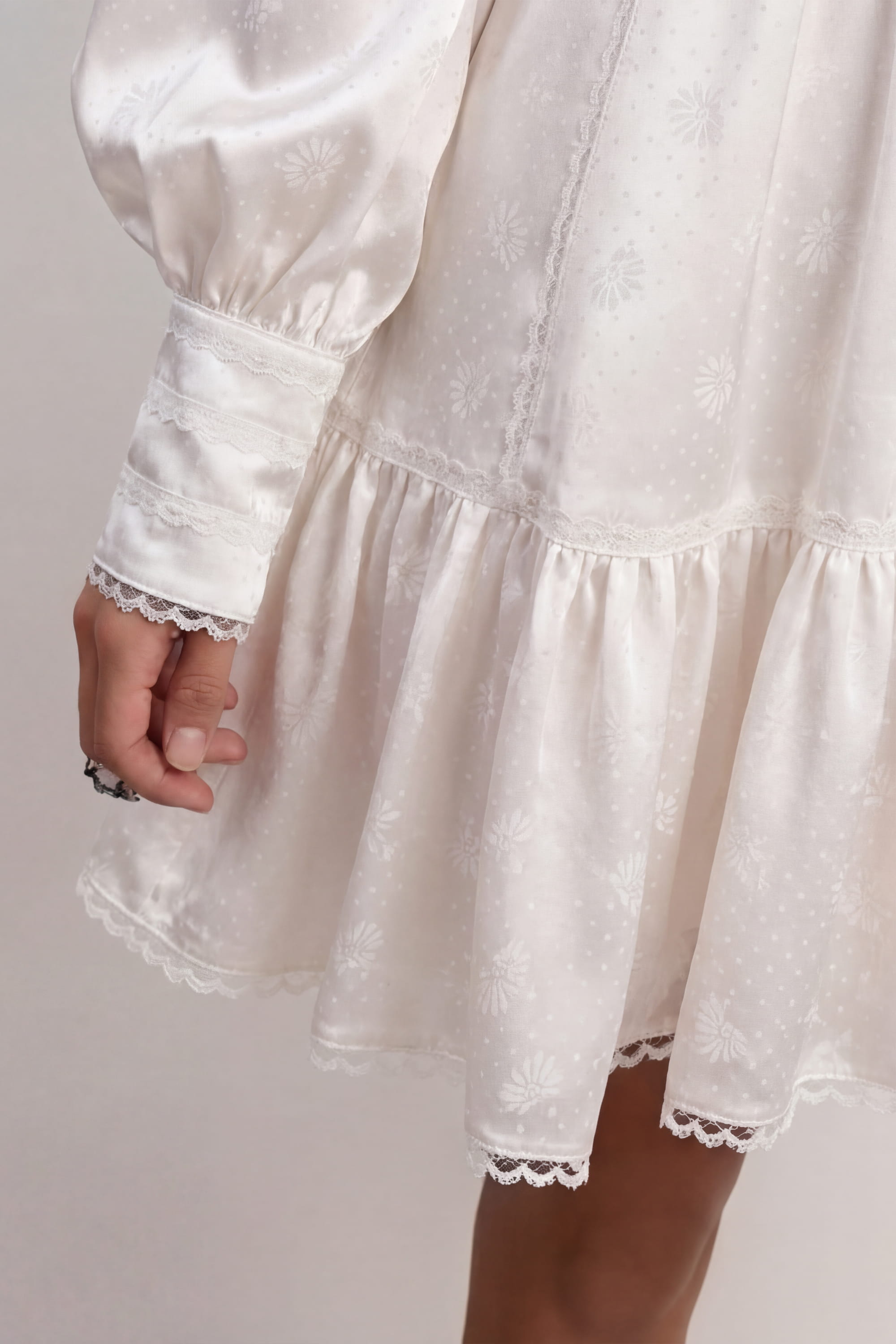 Woman wearing a soft white Wildflower dress with long sleeves and lace details against a plain background, details front view