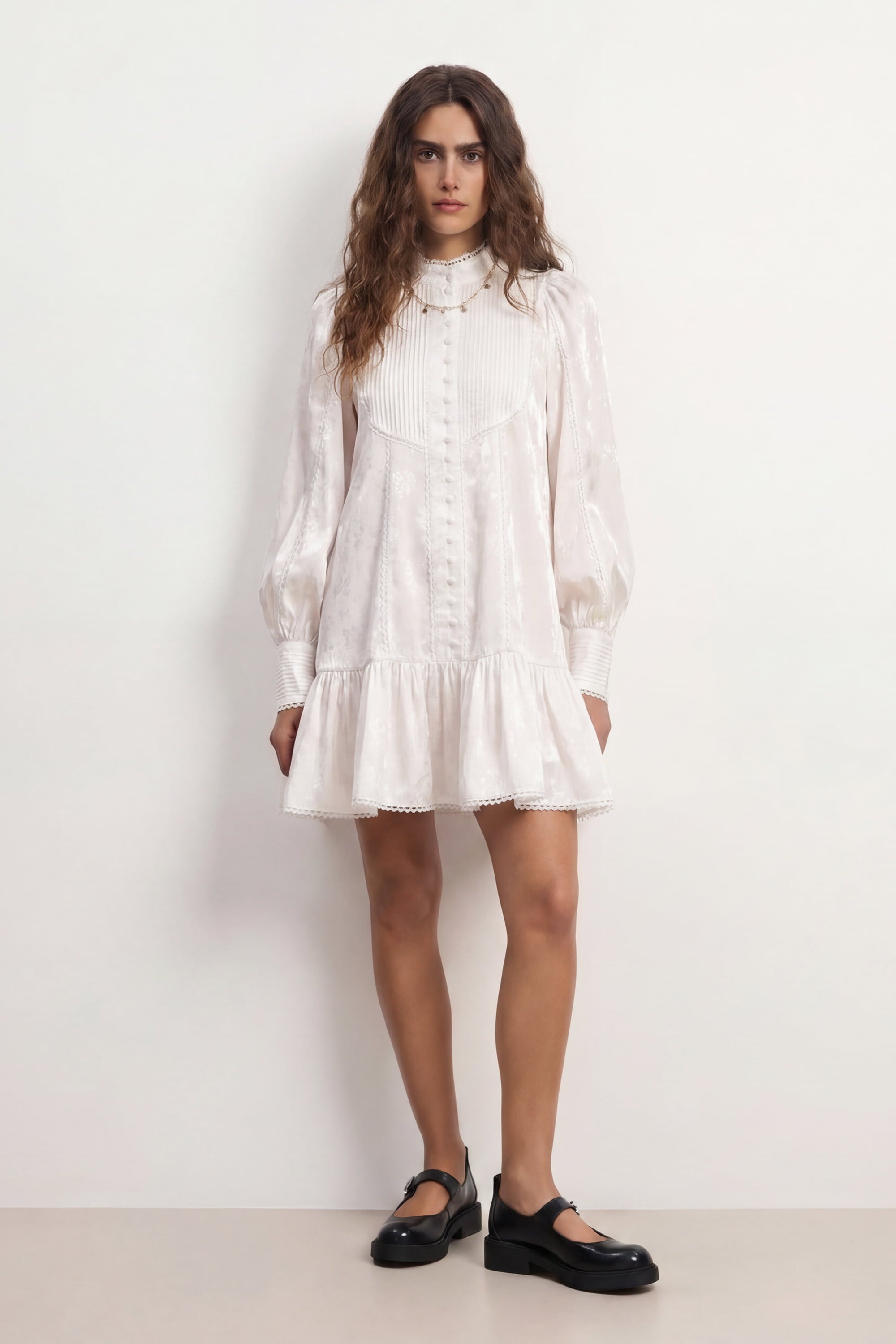 Woman wearing a soft white Wildflower dress with long sleeves and lace details against a plain background, front view